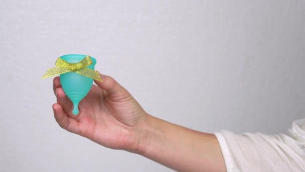 Frauenhände demonstrieren blaue Menstruationstasse mit Goldschleife als Bonus oder Geschenk, persönliches Hygieneprodukt zum Zeitpunkt der Menstruation — Stockvideo