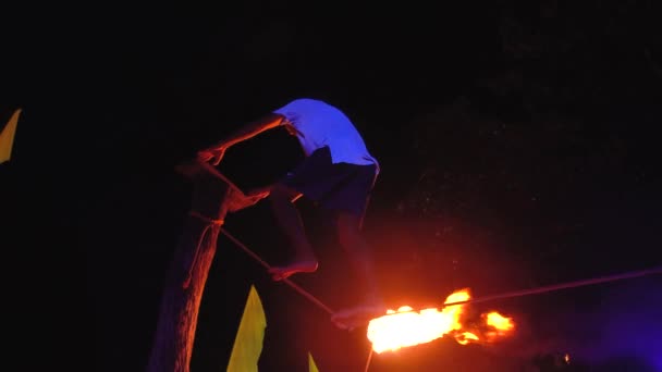 Таиланд, остров Пхи-Пхи, 28 сентября 2019 года: огненное шоу на открытом пляже. Сосредоточенный мужчина-балансировщик стоит на веревке и жонглирует огненными шарами ночью на улице. — стоковое видео