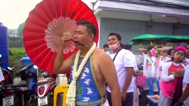 Thajsko, Phuket, 7. října 2019: detailní portrét thajského muže čínského původu s propíchnutou tváří propíchnutou velkým čínským červeným deštníkem na každoročním festivalu Phuket Vegetarian Festival — Stock video