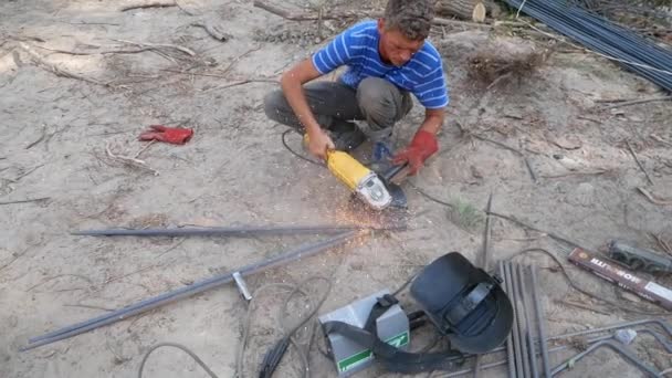 A welder cuts welded rods. The diamond wheel sparks out. The welder holds the cutting metal grinder. Sparks crumble around. City, Kiev. Ukraine. August 15, 2017 — Stock Footage Welder Cuts Welded Rods Diamond Wheel Sparks Out Welder Holds Stock Video