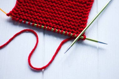 Örgü. Beyaz ahşap arka plan üzerine örgü iğneleri ile örülmüş parlak kırmızı eşarp