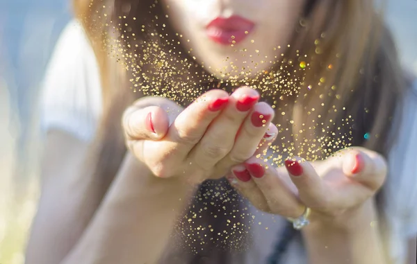 Güzellik genç kadın elini sihirli altın glitter toz üfleme.
