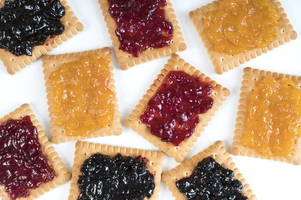 Some dry biscuits with jam on a white surface