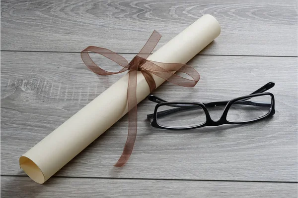 Masanın üzerinde kırmızı kurdeleyle bağlanmış bir çift gözlüklü diploma.