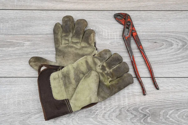 a pipe wrench and a pair of work gloves on a wooden table