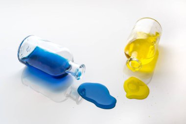 Sarı ve mavi sıvı sızıntısı tarafından küçük cam şişe beyaz bir yüzeye