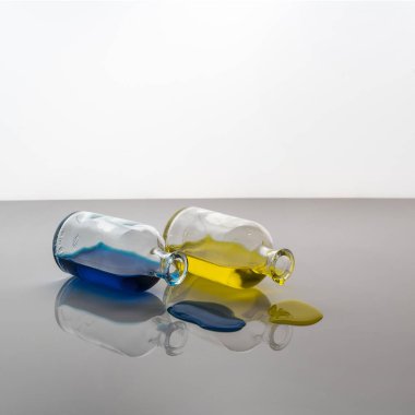 Sarı ve mavi sıvı sızıntısı tarafından küçük cam şişe beyaz bir yüzeye