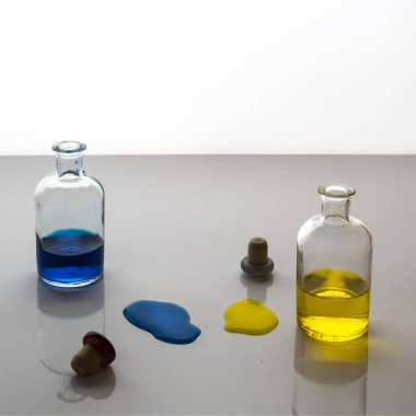 Sarı ve mavi sıvı sızıntısı tarafından küçük cam şişe beyaz bir yüzeye