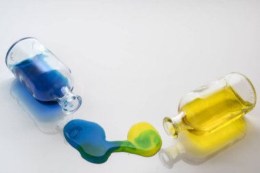 Beyaz bir yüzeyde küçük bir cam şişeyle renkli sıvı dökülmüş.