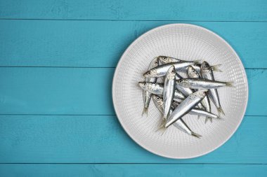 Beyaz ahşap masadaki bir tabağa yerleştirilmiş sardalyalar.