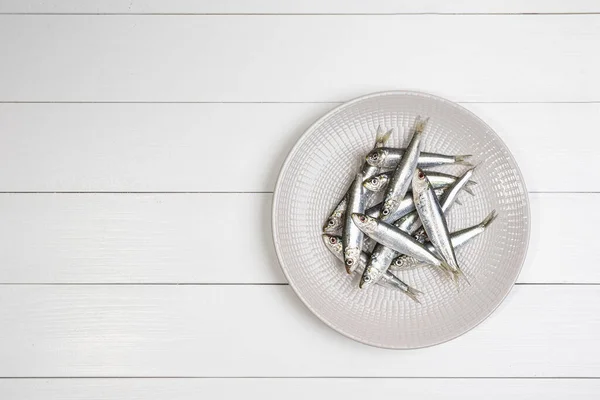 Μερικές Σαρδέλες Τοποθετημένες Ένα Πιάτο Στο Λευκό Ξύλινο Τραπέζι — Φωτογραφία Αρχείου