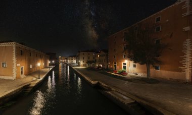 Venedik, İtalya. 8 Ekim 2020. Şehirdeki bir kanalın panoramik gece görüntüsü, gökyüzünde samanyolu olan bir köprüden alındı..