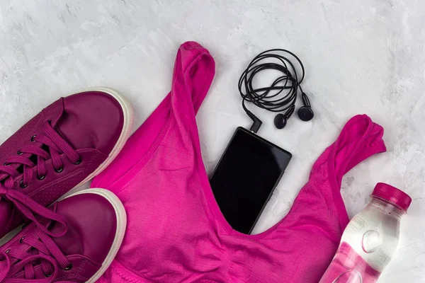 top view sport fashion clothing and accessories set , bright pink color, sneakers, bra, water bottle, smartphone and headphones concrete background