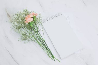 Üstten Görünüm boş beyaz defter ve boquet mermer bir zemin üzerine karanfil ve gypsophila çiçek