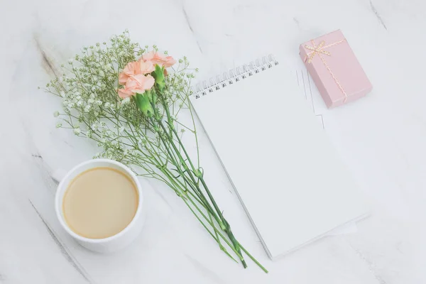 Üstten Görünüm boş beyaz defter, kahve fincanı, hediye kutusu ve boquet mermer bir zemin üzerine karanfil ve gypsophila çiçek