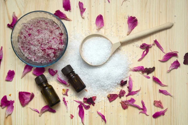 omemade scrub for body,sea salt in wooden spoon, aroma oil, rose petals on wooden background. Spa concept.