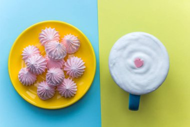 kalp şeklinde pembe şeker ve plaka ile parlak bir arka plan üzerinde beze kakaolu krem şanti ile mavi kupa süslenmiş.