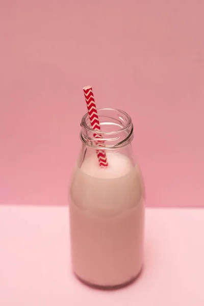 粉红色的草莓奶昔在一个瓶子与鸡尾酒秸秆在粉红色的背景 — 图库照片