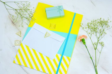 Üstten Görünüm boş beyaz zarf, hediye kutuları, parlak klasör ve mermer bir masaya çiçek