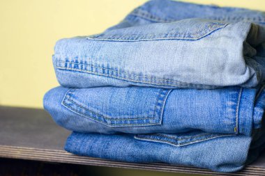 bir ahşap raf sarı duvar arka plan için mavi jeans yığını