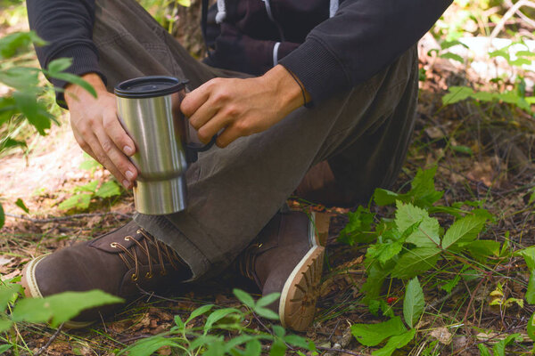 man traveler at a halt with a mug of hot drink in the forest