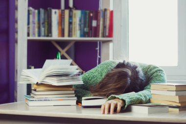 bir yığın kitap ve eğitim materyalleri, bulanık bir kitaplık ve arka planı için bir pencere ortasında bir masada yeşil kazaklı kadın uyur