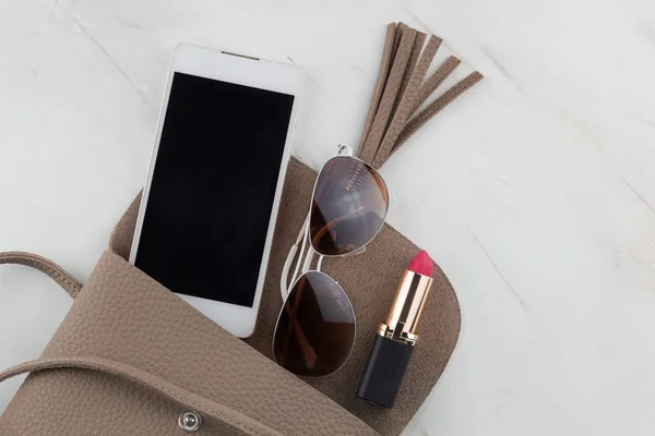 Üstten Görünüm içeriğini kadınlar çanta ruj, telefon ve mermer masada açık bir çanta içinde güneş gözlüğü