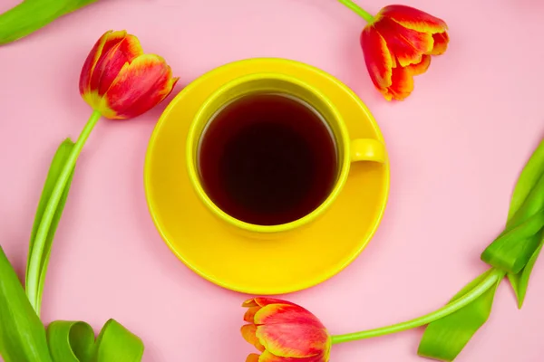 yellow  coffee cup and red tulips layout  on pastel pink background, top view