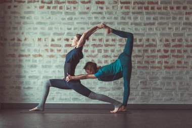iki güzel beyaz kadın Partner yoga yoga Studio tuğla duvar karşısında yapıyor