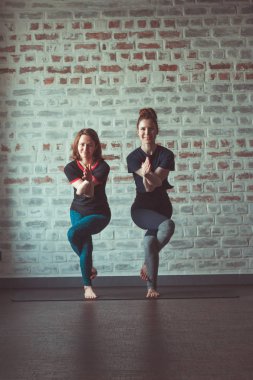 iki güzel beyaz kadın Partner yoga yoga Studio tuğla duvar karşısında yapıyor