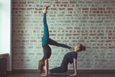 iki güzel beyaz kadın Partner yoga yoga Studio tuğla duvar karşısında yapıyor