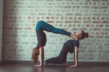 iki güzel beyaz kadın Partner yoga yoga Studio tuğla duvar karşısında yapıyor