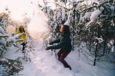 genç kadın ve genç adam rüzgârla oluşan kar yığını ağaçlar arasında kartopu oynayan karla kaplı