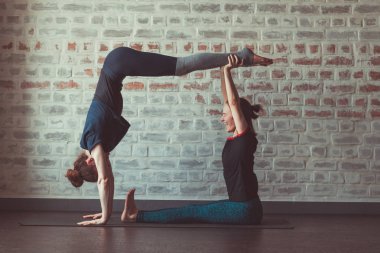 iki güzel beyaz kadın Partner yoga yoga Studio tuğla duvar karşısında yapıyor