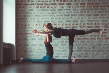 iki güzel beyaz kadın Partner yoga yoga Studio tuğla duvar karşısında yapıyor