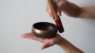 bir erkeğin ellerine tahta bir sopa ile bir Tibet singing kase beyaz duvara karşı oynarken, yakın çekim