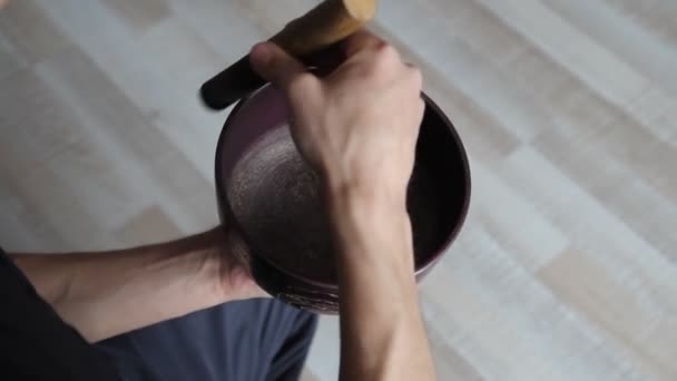 A férfi kezet játszik egy tibeti éneklő bowl, egy fa bottal közelről felülnézet — Stock videók