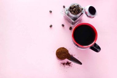 üst görünümü kahve fincanı, zemin kahve çekirdekleri ve pembe bir arka plan üzerinde kahve çekirdekleri ile kavanoz kaşığı
