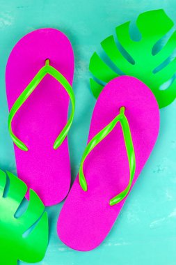 üst görünüm parlak pembe terlik ve kağıt mavi arka planda tropikal Monstera yaprak kesilmiş