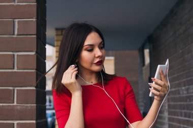 Kırmızı elbise kırmızı ruj ile güzel genç kadın telefon ve kulaklıklar kullanır