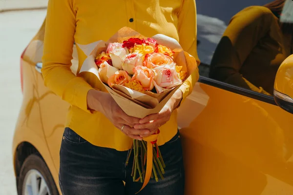 woman in yellow blouse with gentle bouquet of yellow roses near yellow car
