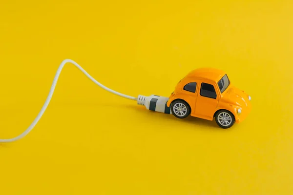 small toy car with charging cable isolated on yellow background , electric car concept and eco-friendly lifestyle