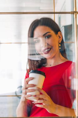 Kırmızı elbise tutarak güzel bir kadın bir kahve dükkanında kahve bardağı almak, cam üzerinden vurdu