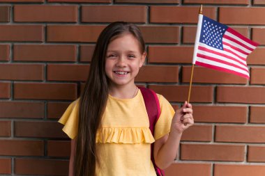 sevimli küçük kız gülümseyen ve tutan Amerikan bayrağı ayakta ayakta tuğla duvara karşı