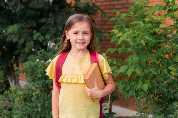 Portrait Little Beautiful Girl Backpack Holding Book Smiling Background Brick — Stock Photo, Image