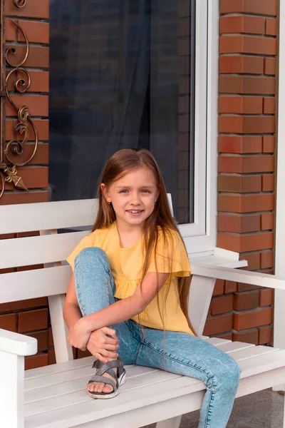 ベンチに座ってカジュアルな服を着て長いブロンドの髪を持つ幸せな美しい少女の肖像画 — ストック写真