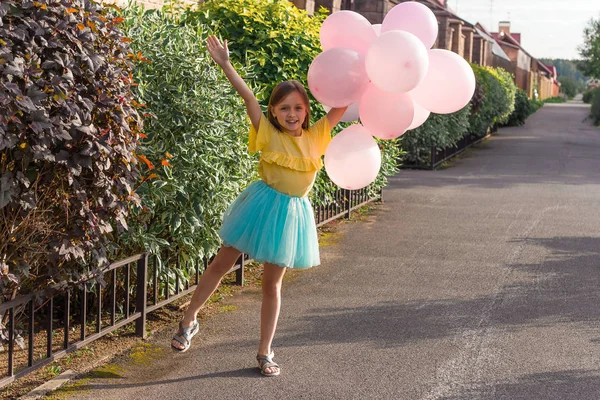 cute little girl in yellow shirt and blue skirt smiling and holding a lot of  balloons ,happy childhood and summer concept