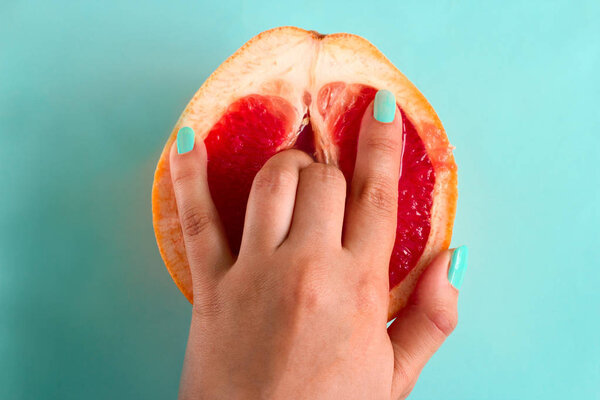 two fingers in a grapefruit isolated on a blue background top view sex concept