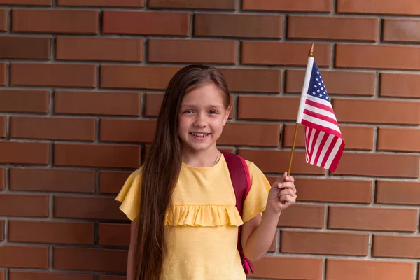 レンガの壁に立って立ってアメリカの旗を持って微笑んで持っているかわいい女の子 — ストック写真