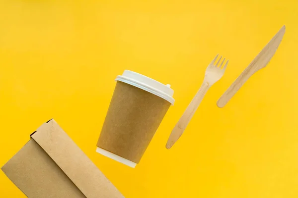 eco friendly food packaging set  disposable  cup, box,spoon and fork flying  on a yellow  background